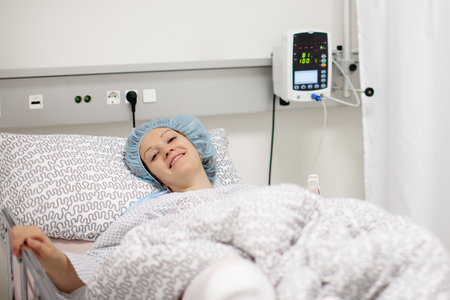 Young patient recovering after surgery in post operative care room in modern hospital. Woman with...