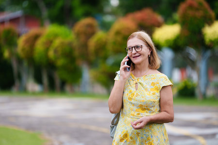 Senior woman with mobile phone on city street. Beautiful stylish lady walking in sunny summer city. Travel and relax time during retirement. Female calling and texting on cell phone.の写真素材