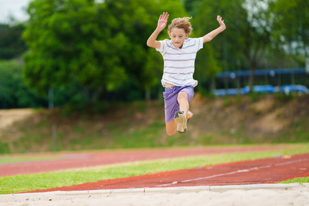Kids long jump athletics training. Child jumping in sand pit on school stadium. Healthy outdoor exercise for children. Young athlete exercising. Sport for young boy.の写真素材