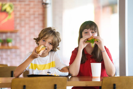 Kids eating fastfood. Unhealthy junk food. Children eat burger, chips and chicken nuggets in fast food cafe. Boy and girl having lunch. Quick snack for family. French fries and hamburger for dinner.の写真素材
