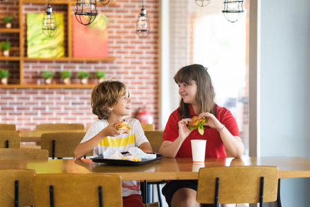 Kids eating fastfood. Unhealthy junk food. Children eat burger, chips and chicken nuggets in fast food cafe. Boy and girl having lunch. Quick snack for family. French fries and hamburger for dinner.の写真素材