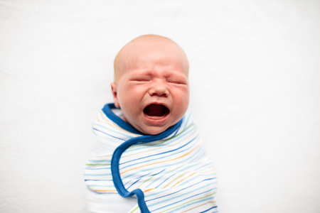 Swaddling newborn child. Baby in swaddle blanket. Tired crying baby wrapped for sleep. Hungry infant in bed.の写真素材