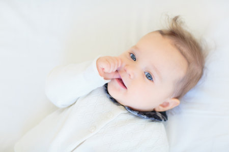 Adorable baby in white sunny bedroom. Newborn child relaxing in bed. Nursery for young children....