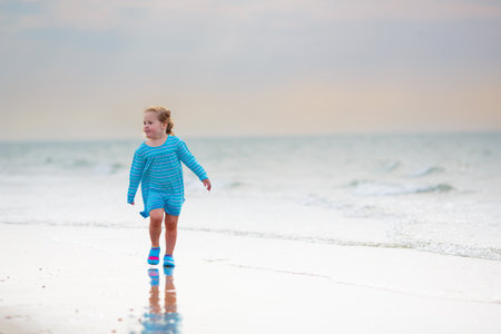 Kids playing on tropical beach. Children swim and play at sea on summer family vacation. Sand and water fun, sun protection for young children. Little baby running and jumping at ocean shore.の写真素材