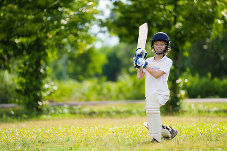 Kids playing cricket in summer park. Boy with bat and ball on cricket pitch. Helmet and guard for safe game. Sport for active child. Cricket club for school children. Sports activity and exercise.の写真素材