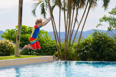 Group of kids jump into swimming pool. Summer water fun. Children play in outdoor pool. Summer family vacation with young kid. Holiday in tropical resort. Travel with child.の写真素材