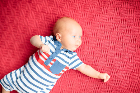 Adorable baby on knitted colorful blanket in white sunny bedroom. Newborn child relaxing in bed. Nursery for young children. Winter warm textile and bedding for kids. Family morning at home.の写真素材