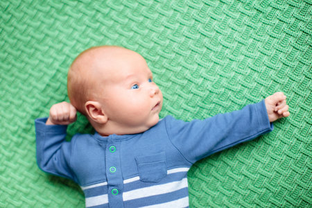Adorable baby on knitted colorful blanket in white sunny bedroom. Newborn child relaxing in bed. Nursery for young children. Winter warm textile and bedding for kids. Family morning at home.の写真素材