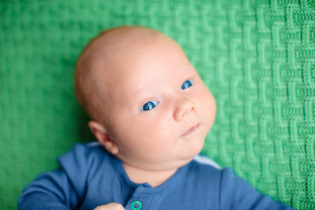 Adorable baby on knitted colorful blanket in white sunny bedroom. Newborn child relaxing in bed....