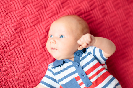 Adorable baby on knitted colorful blanket in white sunny bedroom. Newborn child relaxing in bed. Nursery for young children. Winter warm textile and bedding for kids. Family morning at home.の写真素材