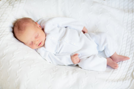 Adorable baby in white sunny bedroom. Newborn child relaxing in bed. Nursery for young children....