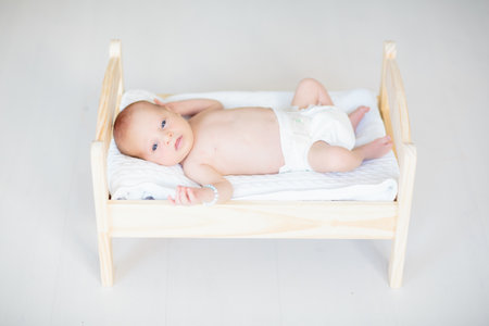 Adorable baby in white sunny bedroom. Newborn child relaxing on toy bed. Nursery for young children. Textile and bedding for kids. Family morning at home. New born kid during tummy time with toy bear.の写真素材