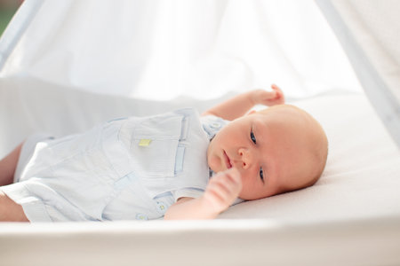 Adorable baby in white sunny bedroom. Newborn child relaxing in bed. Nursery for young children. Textile and bedding for kids. Family morning at home. New born kid during tummy time with toy bear.の写真素材