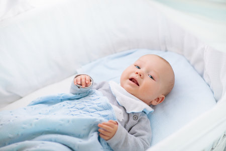 Adorable baby in crib in white sunny bedroom. Newborn child relaxing in bed. Nursery for young children. Textile and bedding for kids. Family morning at home. New born kid during tummy time with toy bear.の写真素材