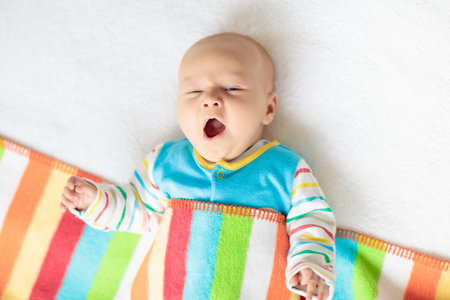 Adorable baby in white sunny bedroom. Newborn child relaxing in bed. Nursery for young children....