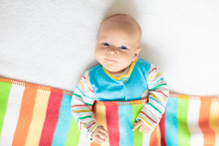 Adorable baby in white sunny bedroom. Newborn child relaxing in bed. Nursery for young children....