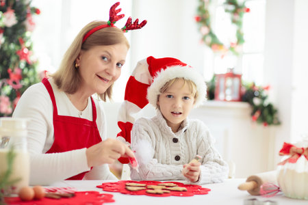 Family baking Christmas cookies. Grandmother and child bake gingerbread pastry. Kids Xmas fun. Little boy in Santa hat making dough for winter cookies. Home holiday decoration.の写真素材