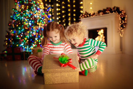 Child decorating Christmas tree at home. Little boy and girl in pajamas with Xmas ornament. Family with kids celebrate winter holidays. Kids decorate living room and fireplace for Christmas.の写真素材
