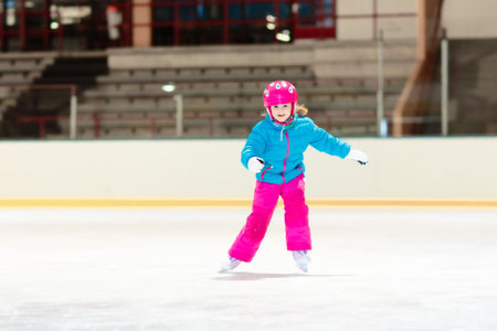 Child skating on indoor ice rink. Kids skate. Active family sport during winter vacation and cold season. Little girl in colorful wear training or learning ice skating. School sport activities and clubsの写真素材