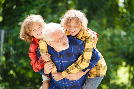 Grandfather and kids in sunny garden. Happy family playing in summer park. Grandpa and children play outdoor. Generation love. Active senior man with little boy. Grandchildren visit grandparents.の写真素材