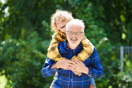 Grandfather and kids in sunny garden. Happy family playing in summer park. Grandpa and children play outdoor. Generation love. Active senior man with little boy. Grandchildren visit grandparents.の写真素材