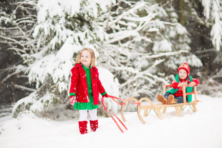 Kids on sleigh in winter forest. Merry Christmas greeting with little kids on sledge. Xmas holiday...