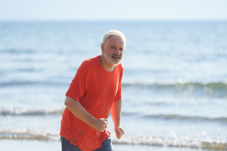 Senior man running on tropical beach. Happy active retirement. Fit retired man exercising on sea side. Vacation and travel in mature age. Jogger on ocean shore.の写真素材