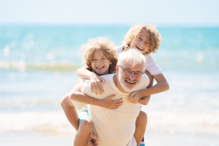 Grandfather and kids play on summer beach. Family day outdoor. Grandparent and grandchildren travel to sea side. Generation love. Active senior man playing with grandson. Happy fit retirement.の写真素材