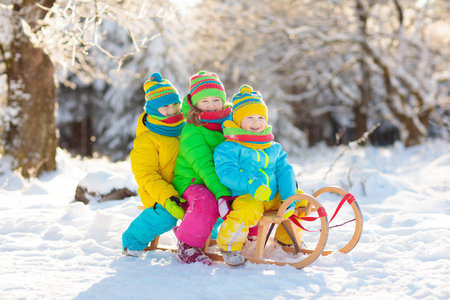 Little girl and boy enjoying sleigh ride. Child sledding. Toddler kid riding a sledge. Children play outdoors in snow. Kids sled in snowy park in winter. Outdoor fun for family Christmas vacation.の写真素材