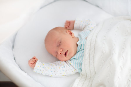 Newborn baby boy in bed. New born child sleeping under a white knitted blanket. Children sleep. Bedding for kids. Infant napping in bed. Healthy little kid shortly after birth. Cable knit textile.の写真素材
