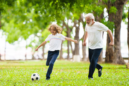 Grandfather and kids play football in sunny park. Happy family playing ball. Grandpa and children play soccer. Generation love. Active senior man with little boy. Grandchildren visit grandparents.の写真素材