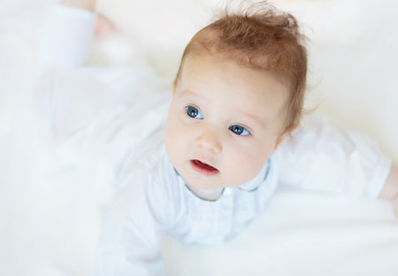 Adorable baby in white sunny bedroom. Newborn child relaxing in bed. Nursery for young children. Textile and bedding for kids. Family morning at home. Child in knitted sweater.の写真素材