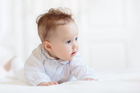 Adorable baby in white sunny bedroom. Newborn child relaxing in bed. Nursery for young children. Textile and bedding for kids. Family morning at home. Child in knitted sweater.の写真素材