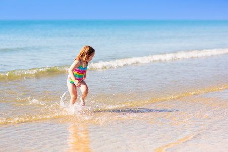 Kids playing on tropical beach. Water splash fun. Little boy splashing in sea waves. Children swim and play on summer family vacation. Sand and water toy, sun protection for young child.の写真素材