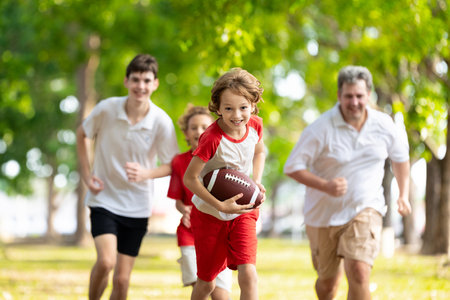 Family playing American football. Kids play rugby in sunny summer park. Father and children throw ball, run and laugh. Healthy outdoor sport activity.の写真素材