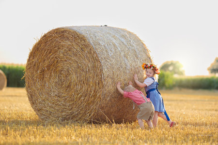 Child in wheat field with bread and pretzel. Kids in traditional German dirndl dress and leather pants in autumn harvest crop field.の写真素材
