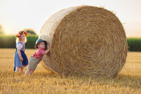 Child in wheat field with bread and pretzel. Kids in traditional German dirndl dress and leather pants in autumn harvest crop field.の写真素材