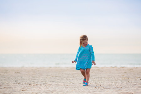 Kids playing on tropical beach. Children swim and play at sea on summer family vacation. Sand and water fun, sun protection for young children. Little baby running and jumping at ocean shore.の写真素材