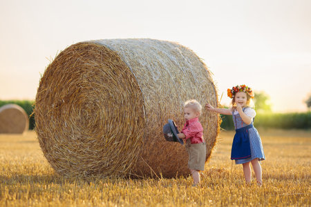 Child in wheat field with bread and pretzel. Kids in traditional German dirndl dress and leather pants in autumn harvest crop field.の写真素材