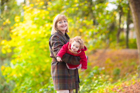 Happy family walking playing in beautiful autumn park on warm sunny fall day. Kids and grandparents play with golden maple leaves.の写真素材