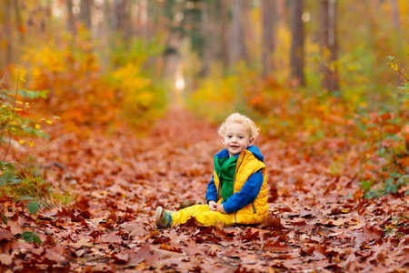 Happy children playing in beautiful autumn park on warm sunny fall day. Kids play with golden maple leaves.の写真素材