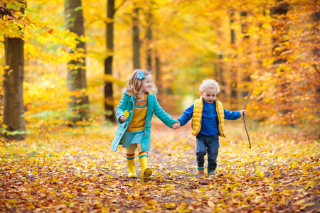 Happy children playing in beautiful autumn park on warm sunny fall day. Kids play with golden maple leaves.の写真素材