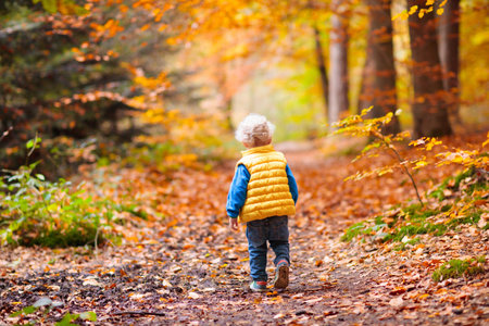 Happy children playing in beautiful autumn park on warm sunny fall day. Kids play with golden maple leaves.の写真素材