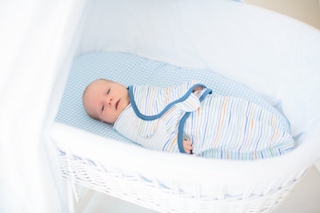 Swaddling newborn child. Baby in swaddle blanket. Tired baby wrapped for sleep. Infant in bed.の写真素材