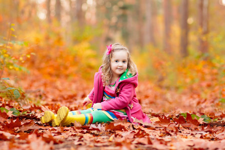 Happy children playing in beautiful autumn park on warm sunny fall day. Kids play with golden maple leaves.の写真素材