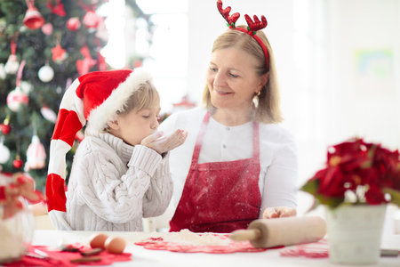 Family baking Christmas cookies. Grandmother and child bake gingerbread pastry. Kids Xmas fun. Little boy in Santa hat making dough for winter cookies. Home holiday decoration.の写真素材