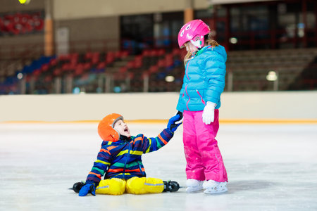Child skating on indoor ice rink. Kids skate. Active family sport during winter vacation and cold season. Little girl and boy in colorful wear training or learning ice skating. School sport clubsの写真素材