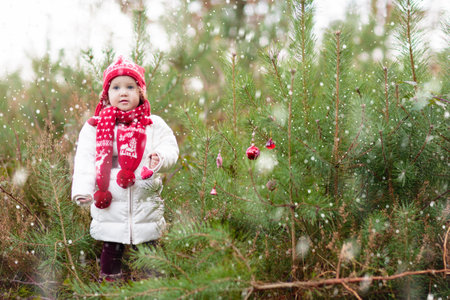Baby in santa costume under Christmas tree. Fun Merry Christmas greeting with little child in gift basket. Xmas present. Child playing outdoor in snow. Kid in winter park.の写真素材
