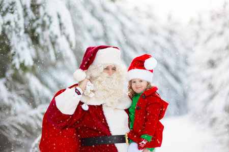 Kids and Santa with Christmas gifts in snowy forest. Children help Santa Claus in snowy park. Fun sleigh ride. Xmas vacation fun. Santa with presents and elves. Winter season holiday.の写真素材