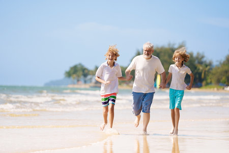 Grandfather and kids play on summer beach. Family day outdoor. Grandparent and grandchildren travel to sea side. Generation love. Active senior man playing with grandson. Happy fit retirement.の写真素材